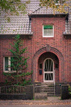 Cozy brick house with an arched doorway surrounded by greenery, perfect for real estate listings.